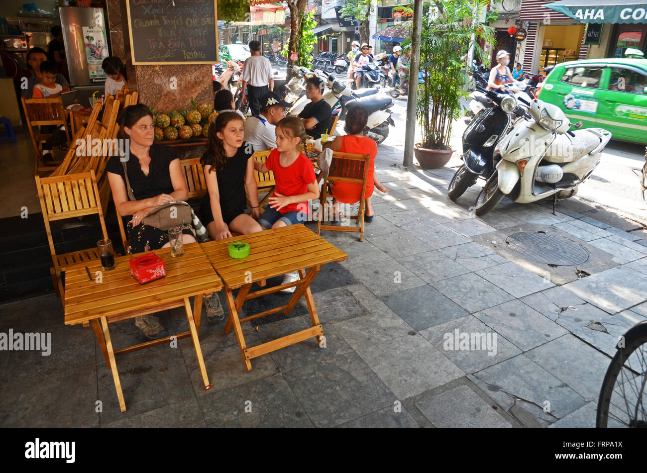 A family of tourists waits for their order in a street-side cafe, Hanoi, Vietnam Stock Photo