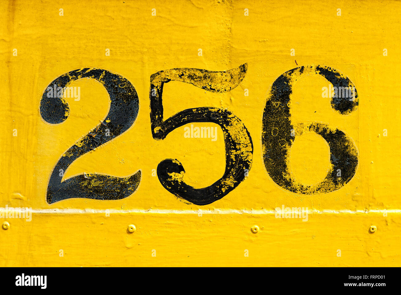 Black number 256 painted over old weathered yellow background with metal texture and rivets Stock Photo