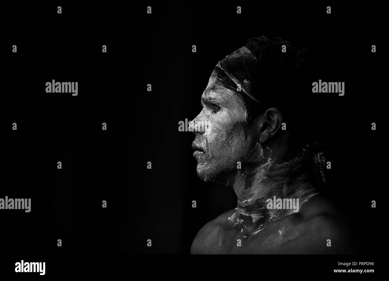 Aboriginal Australian dancer with face paint standing in shadow. Atmospheric black&white profile portrait . Stock Photo