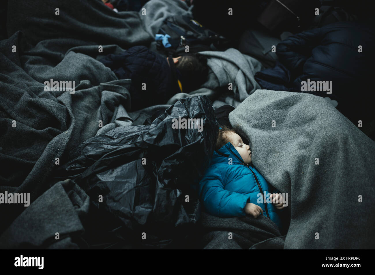 Idomeni refugee camp on Greek Macedonia border, waiting refugees at the checkpoint, a small child sleeps wrapped up in blankets Stock Photo