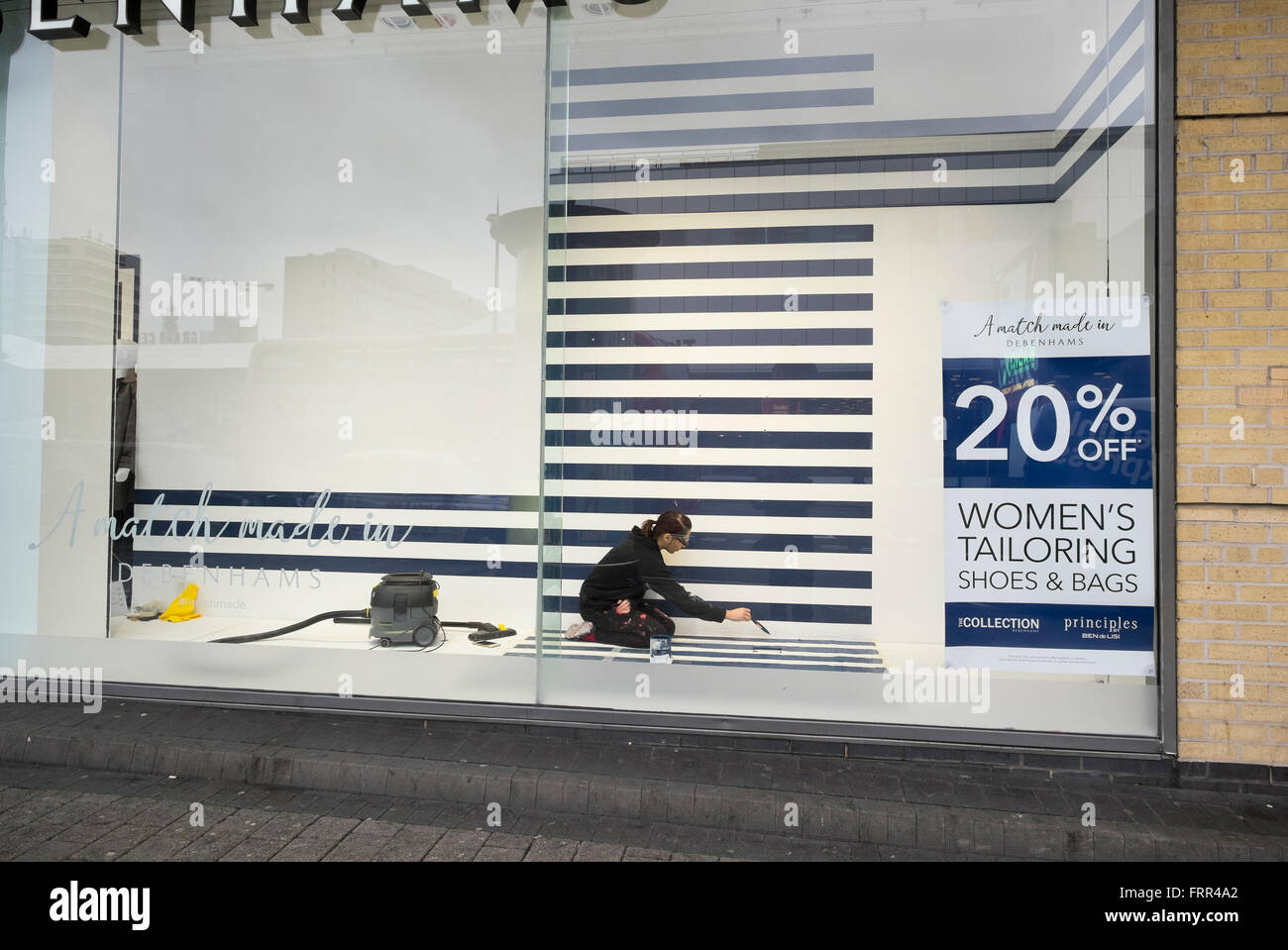A female window dresser painting a display in a window of Debenhams store in Birmingham city centre, West Midlands, England, UK Stock Photo