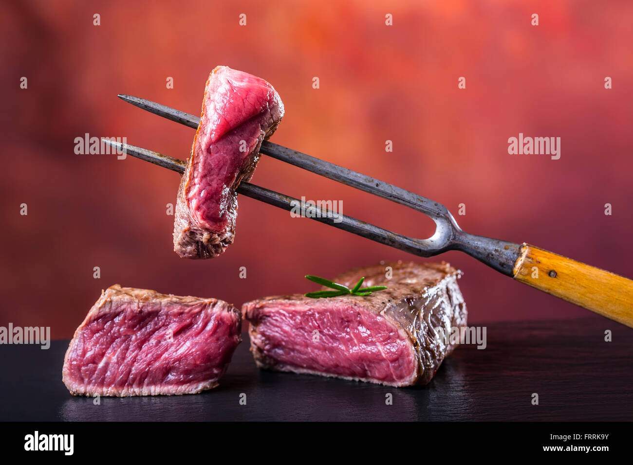 Steak. Grill beef steak. Slices of sirloin beef steak on meat fork on concrete background. Stock Photo