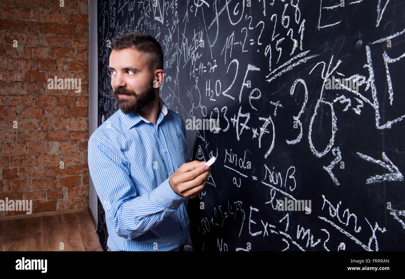 Hipster teacher writing on big blackboard with mathematical symb Stock Photo