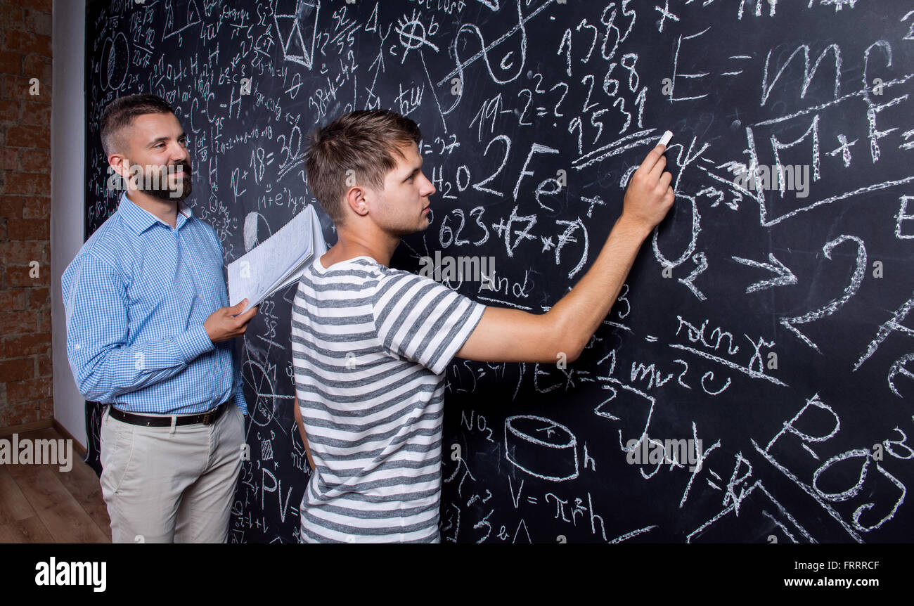 Teacher and student writing on big blackboard with mathematical Stock Photo