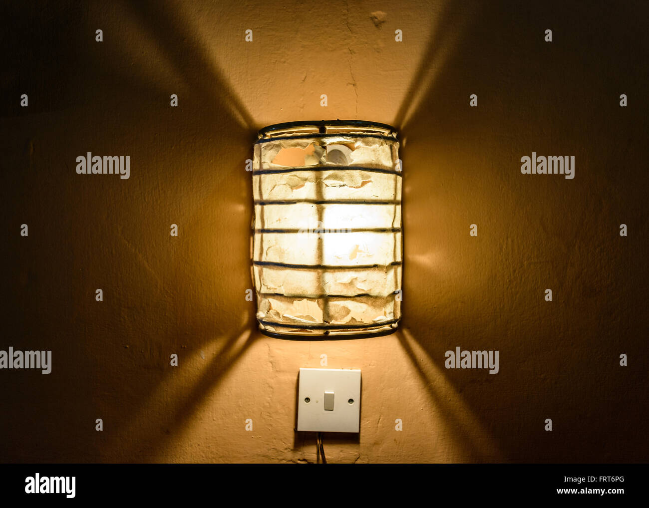 Centered straight on view of illuminated frosted glass flush mount lamp above light switch in dark wall Stock Photo