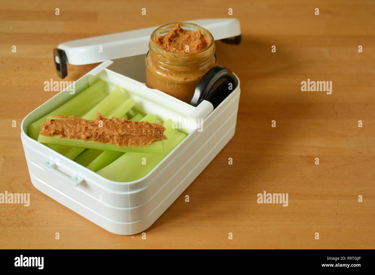 Healthy snacks - snack box containing stalks of celery and jar of peanut butter. Stock Photo