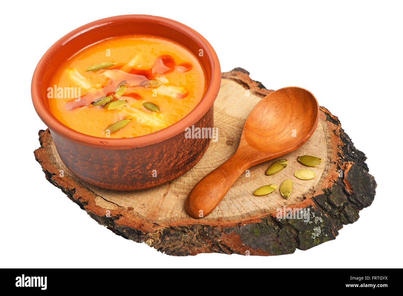 Small ceramic bowl of pumpkin cream soup, wooden spoon, slice of bread and seeds on wood cut isolated on white background, high Stock Photo
