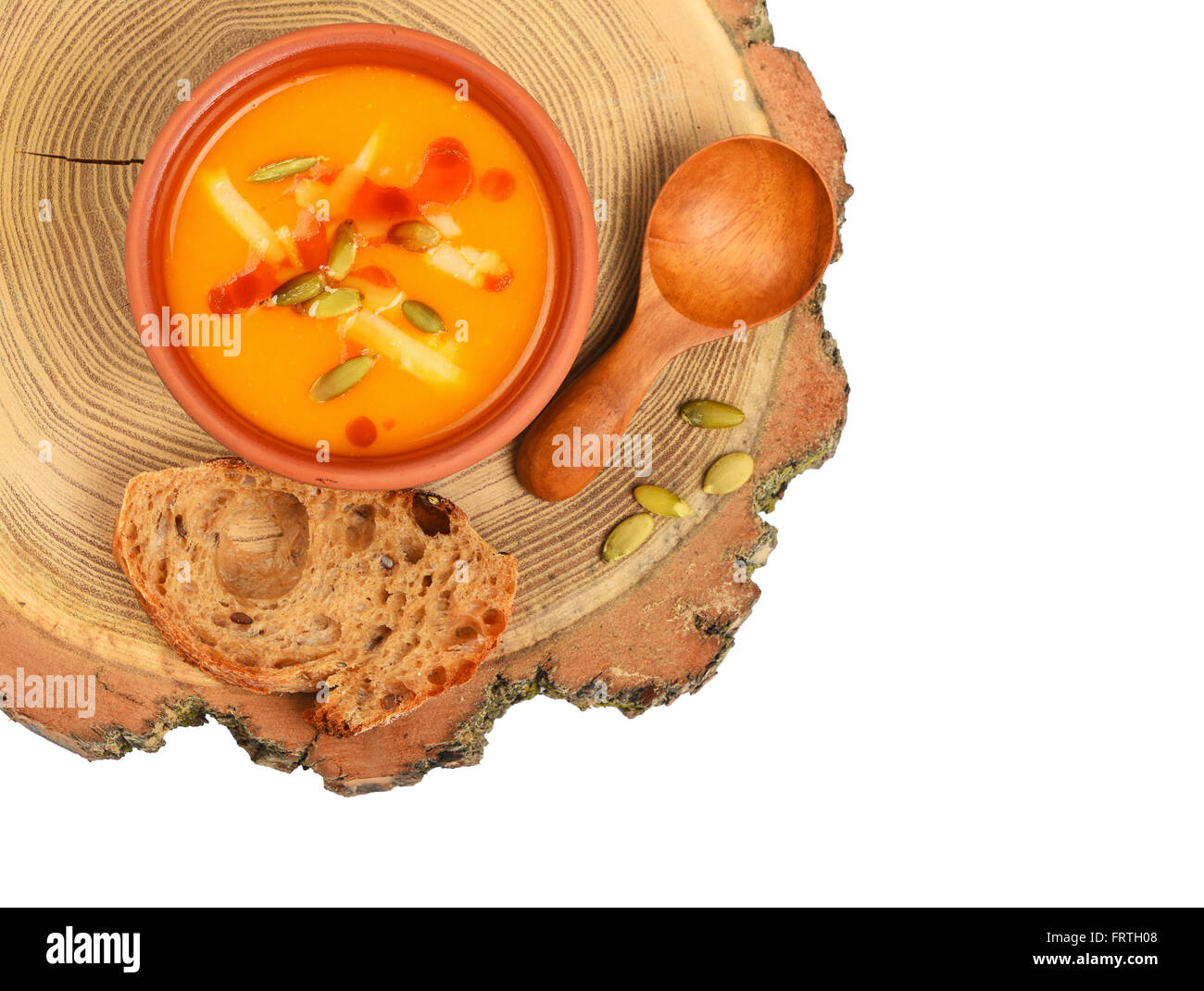 Small ceramic bowl of pumpkin cream soup, wooden spoon, slice of bread and seeds on wood cut isolated on white background, top v Stock Photo