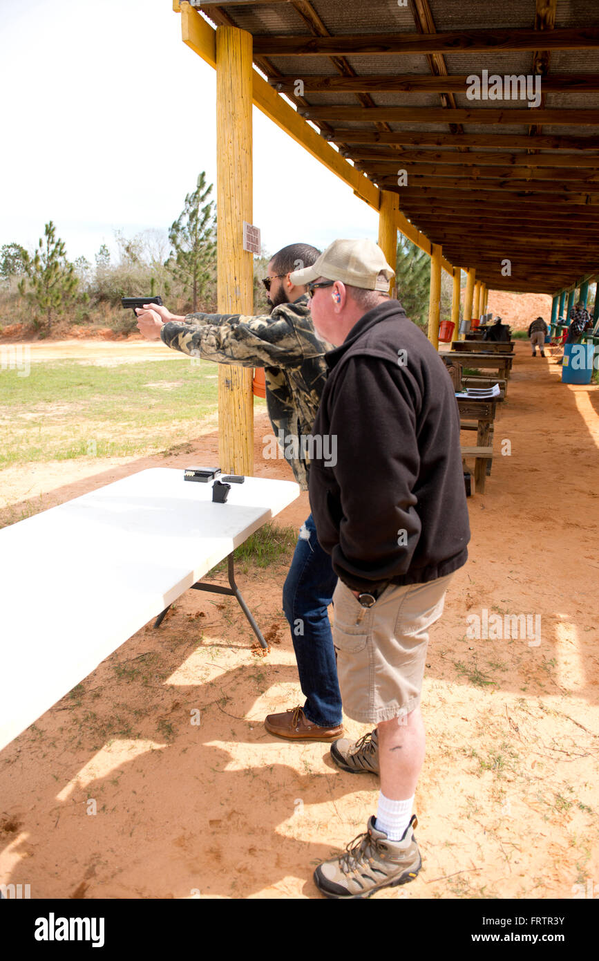 Latin Man Shooting Semi-Auto Handgun while Instructor Looks On Stock Photo