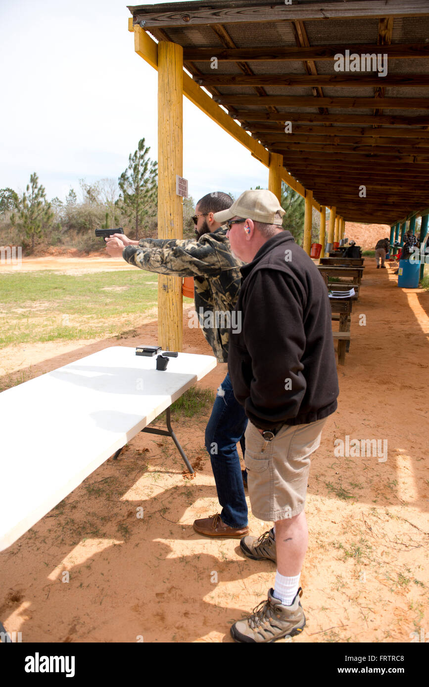 Latin Man Shooting Semi-Auto Handgun while Instructor looks on Stock Photo