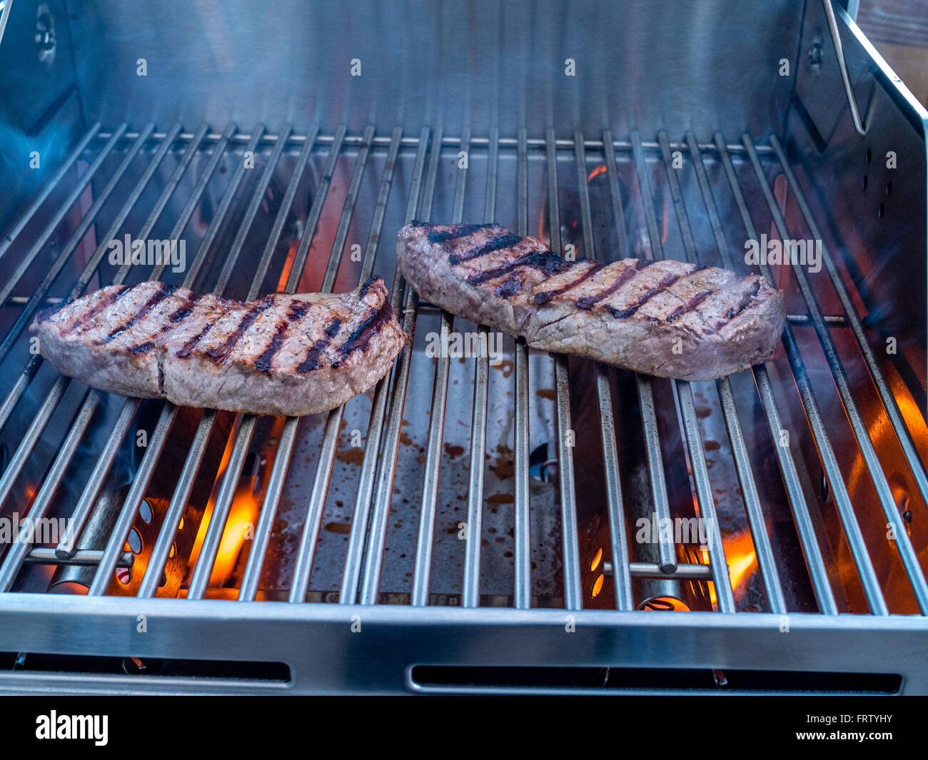 Grilling steaks over flames on a gas grill Stock Photo - Alamy