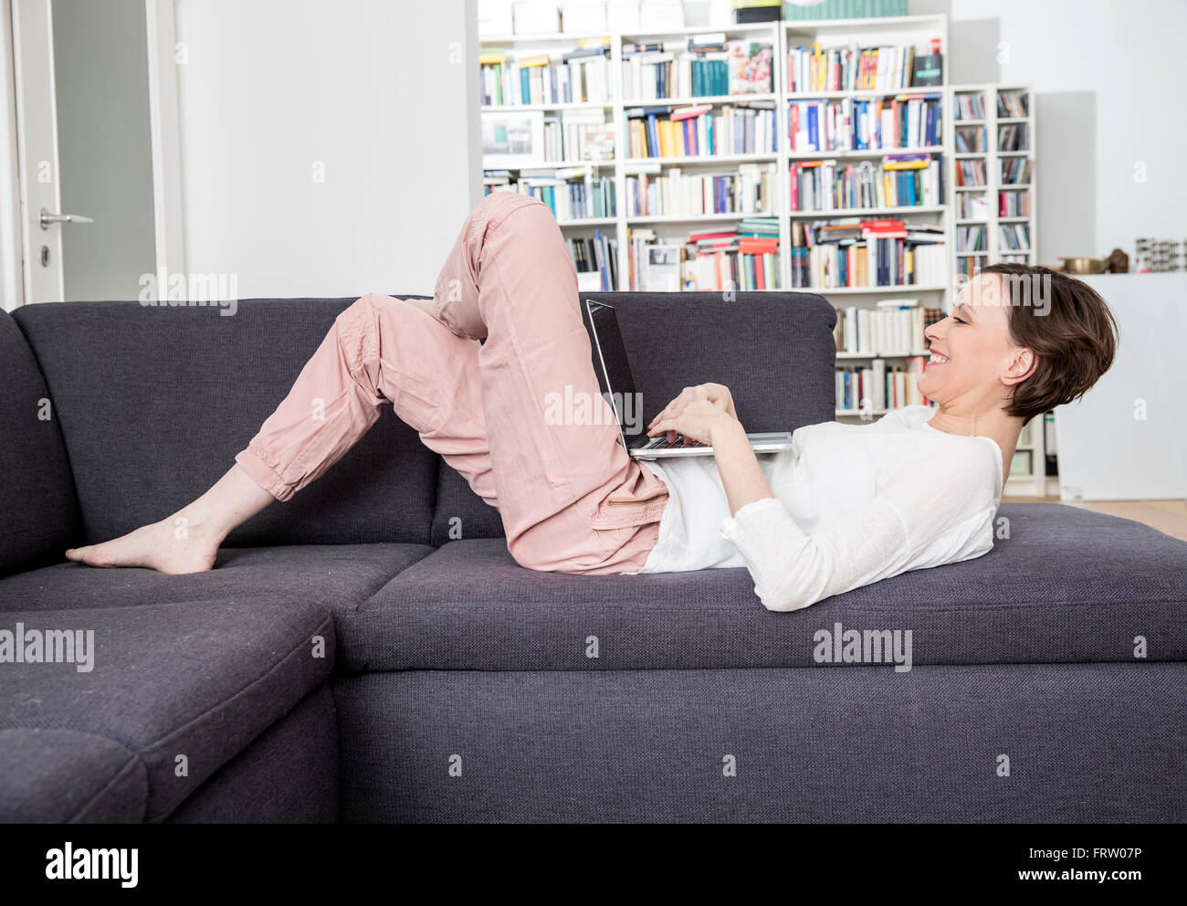 Happy woman lying on couch using laptop Stock Photo - Alamy