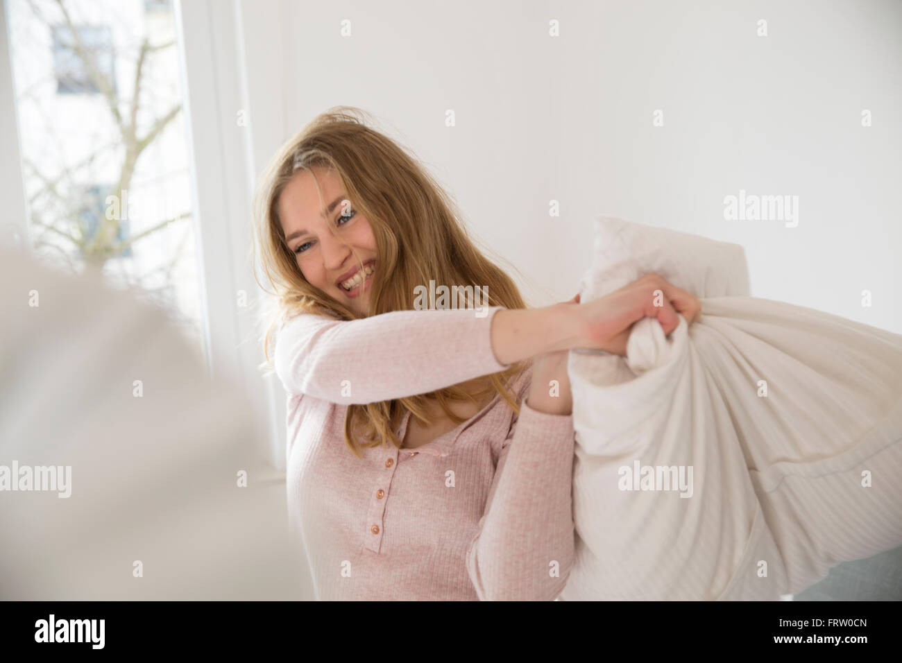 Laughing young woman having pillow fight Stock Photo