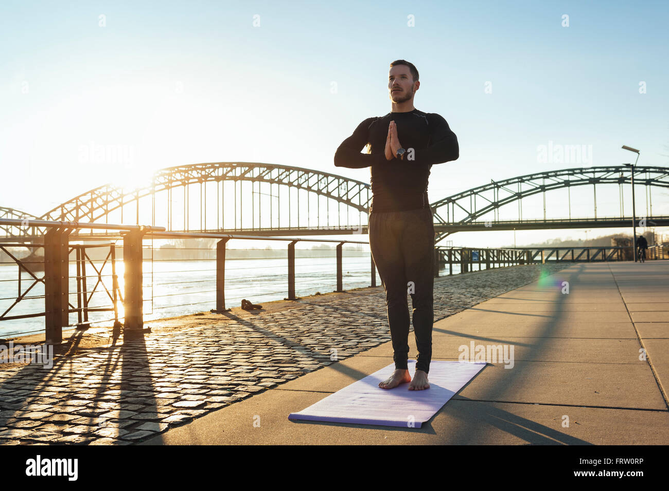 Germany, Cologne, Young man practicing yoga at the riverside Stock Photo