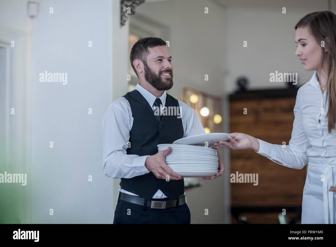 Waiter carrying stack of plates to waitress Stock Photo Alamy