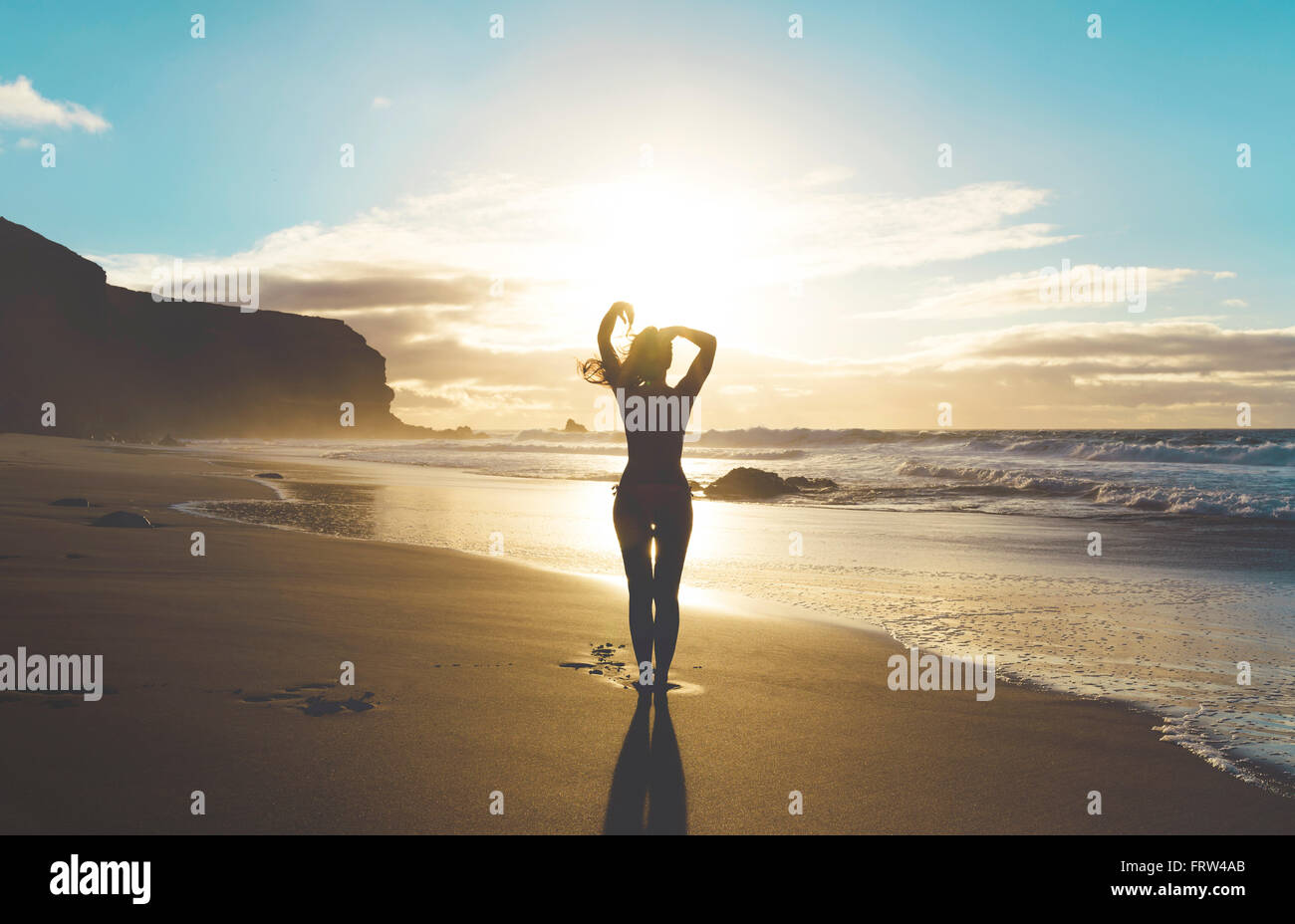 Woman standing on the beach with hands on head at sunset Stock Photo ...