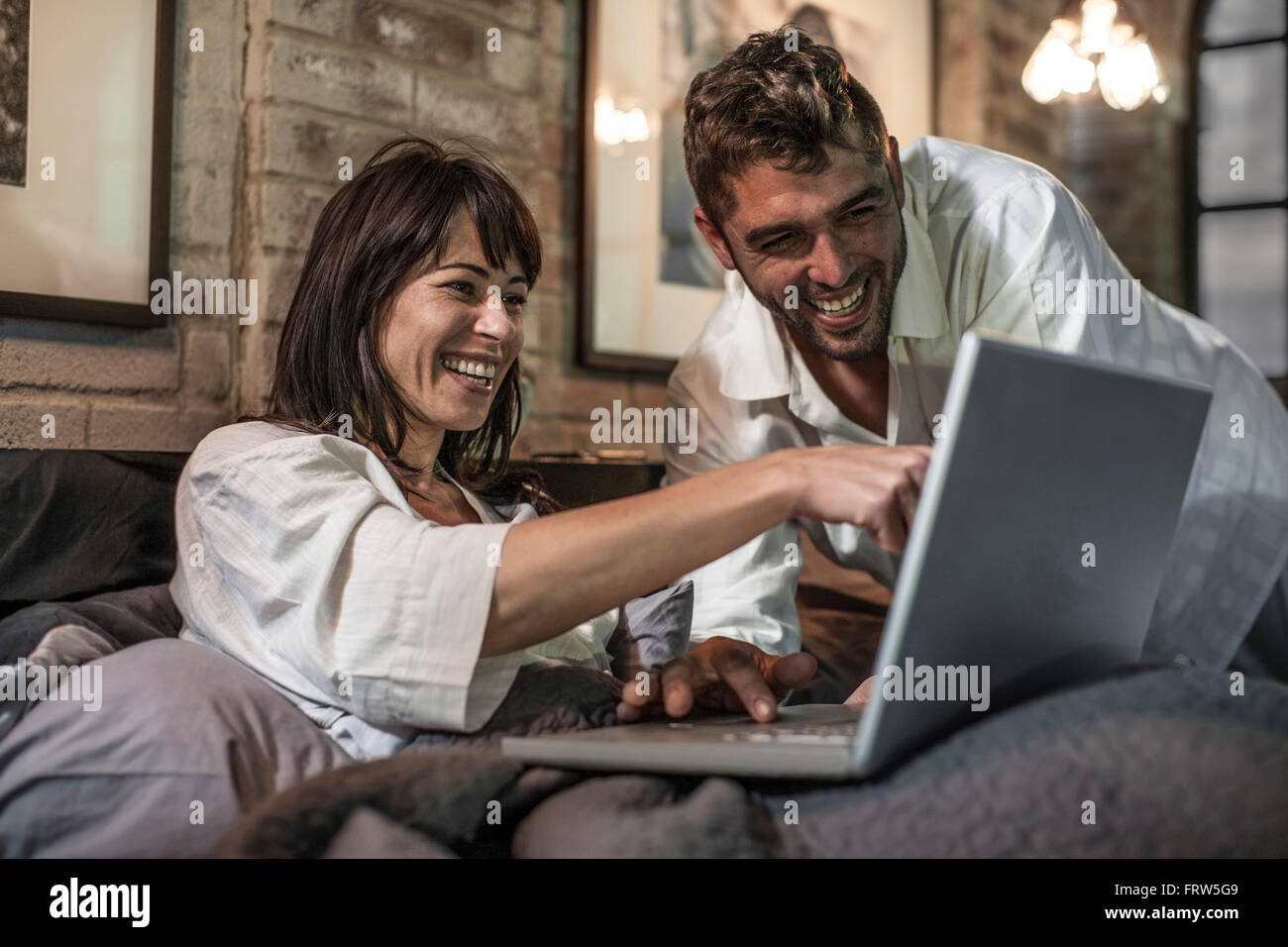 Happy couple together in bed looking at laptop Stock Photo - Alamy