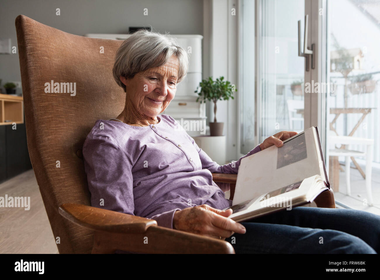 Portrait of senior woman sitting on armchair at home watching photo ...