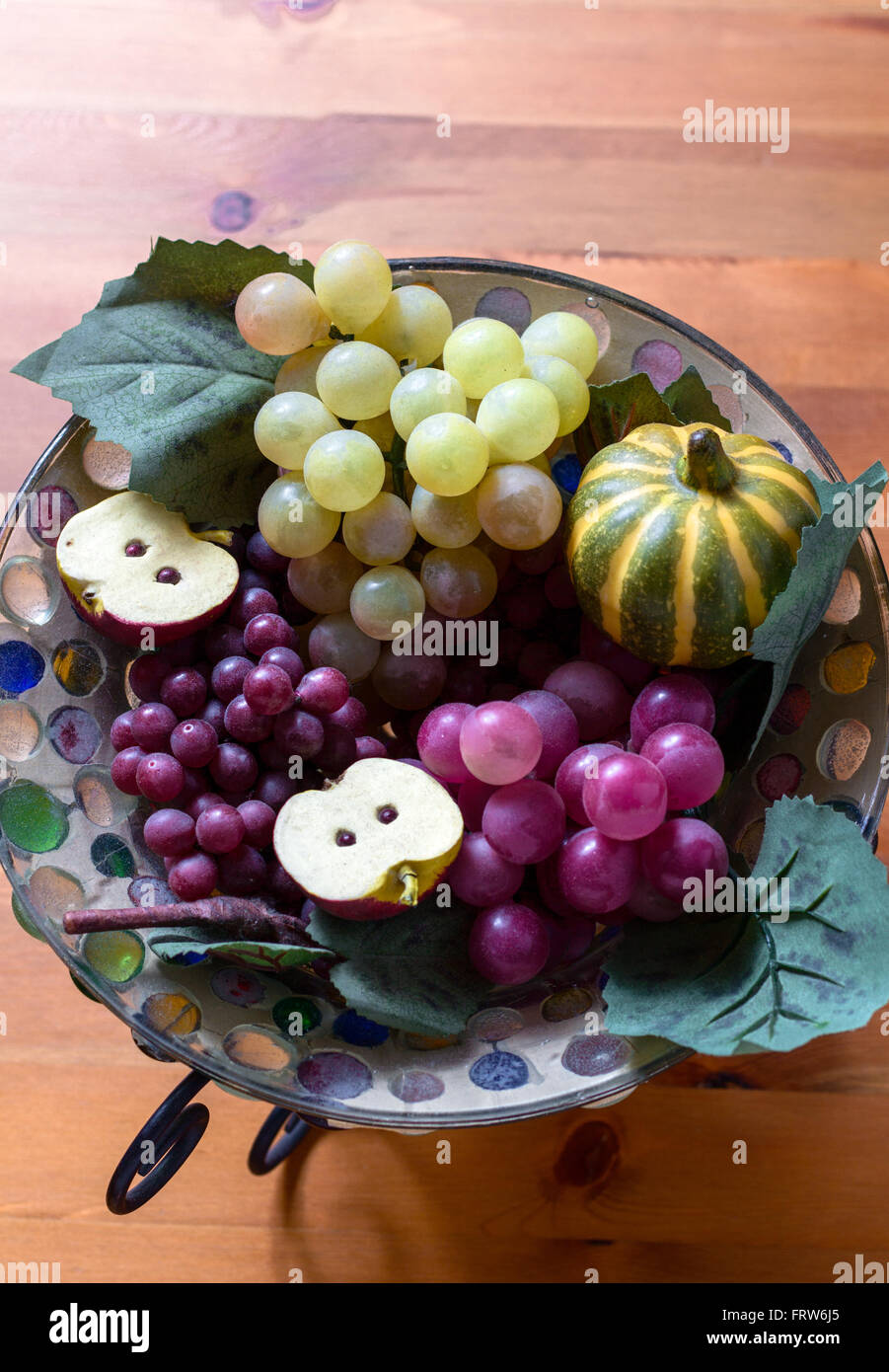 Close-up of artificial grape bunches, apple and pumpkin in glass plate on wooden table. From above Stock Photo