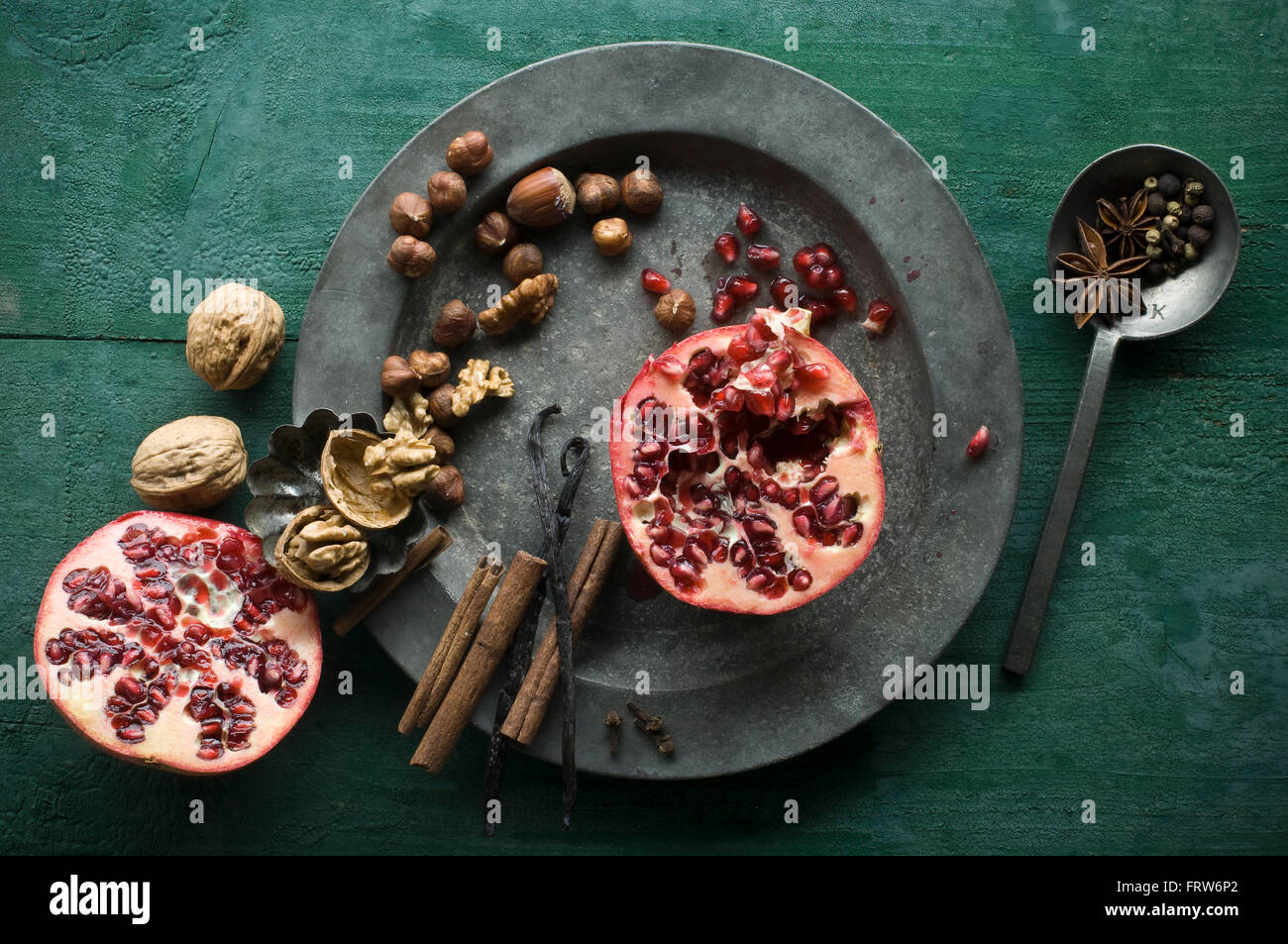 Two halves of pomegranate, different spices and nuts on tin plate Stock Photo