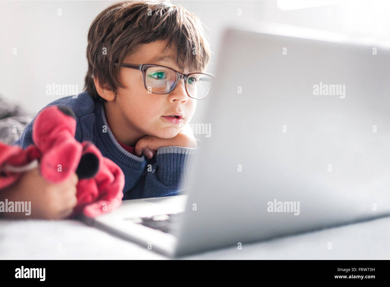 Portrait of little boy wearing oversized glasses looking at laptop Stock Photo