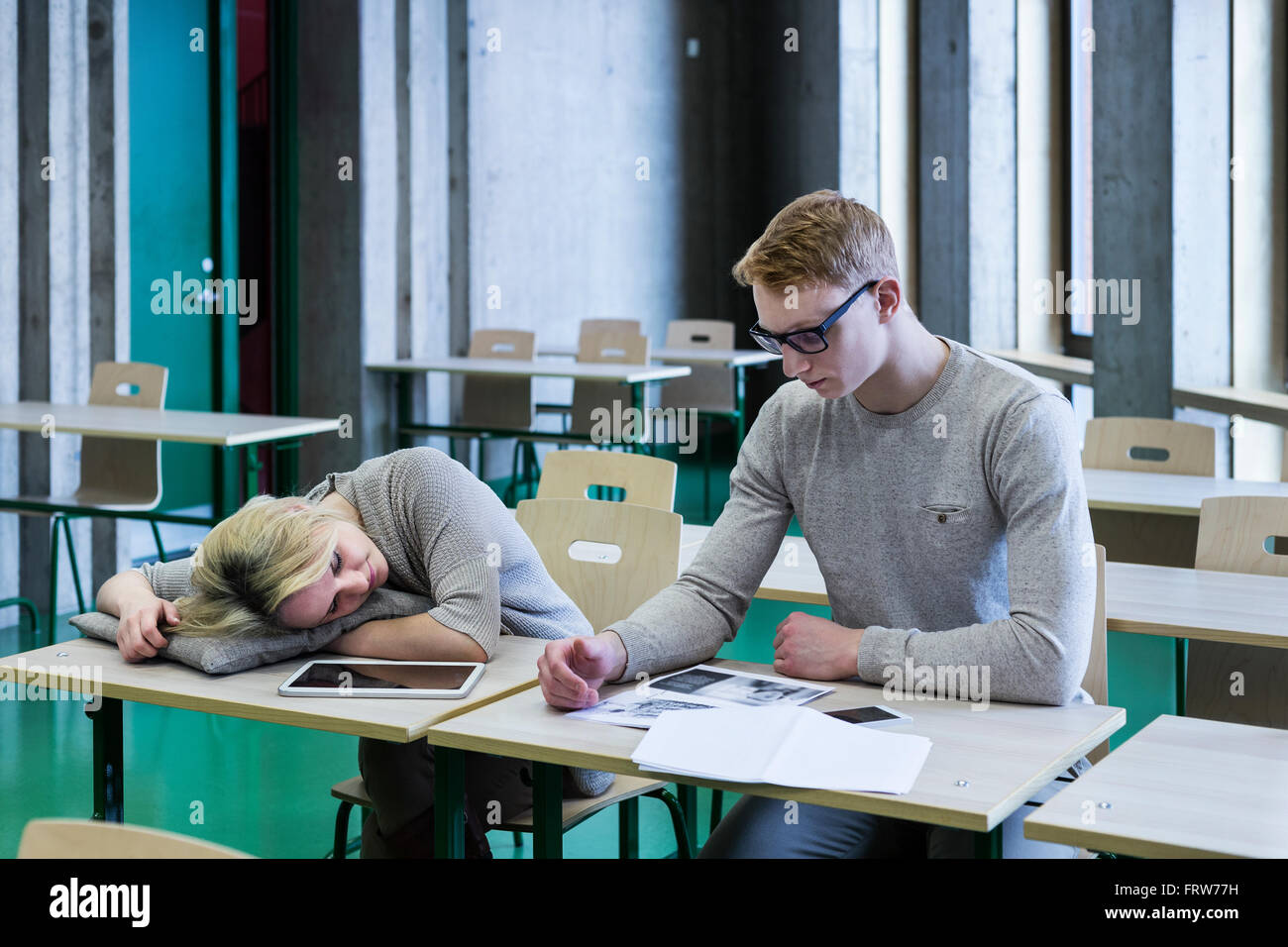 Two students in classroom with woman sleeping on desk Stock Photo