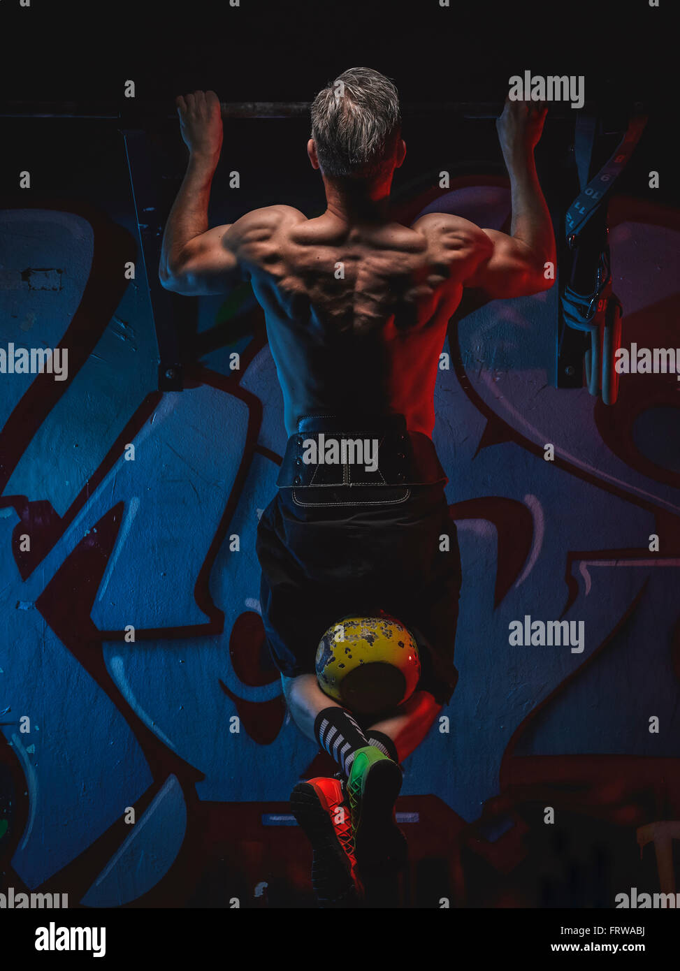 Mature crossfit athlete doing chin-ups with kettlebell Stock Photo
