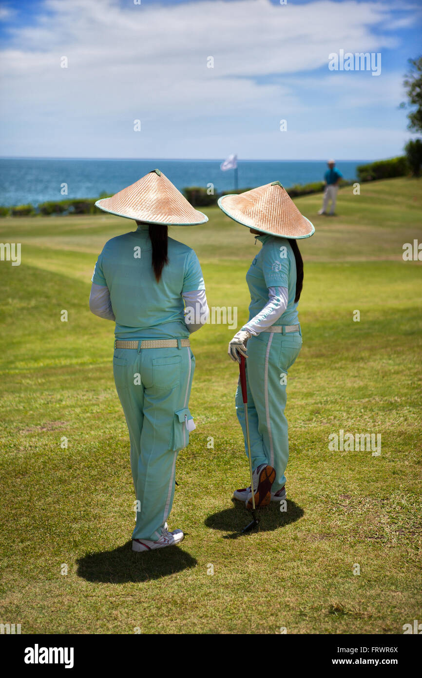 BALI, INDONESIA Two caddies with straw hats on a golf course Stock