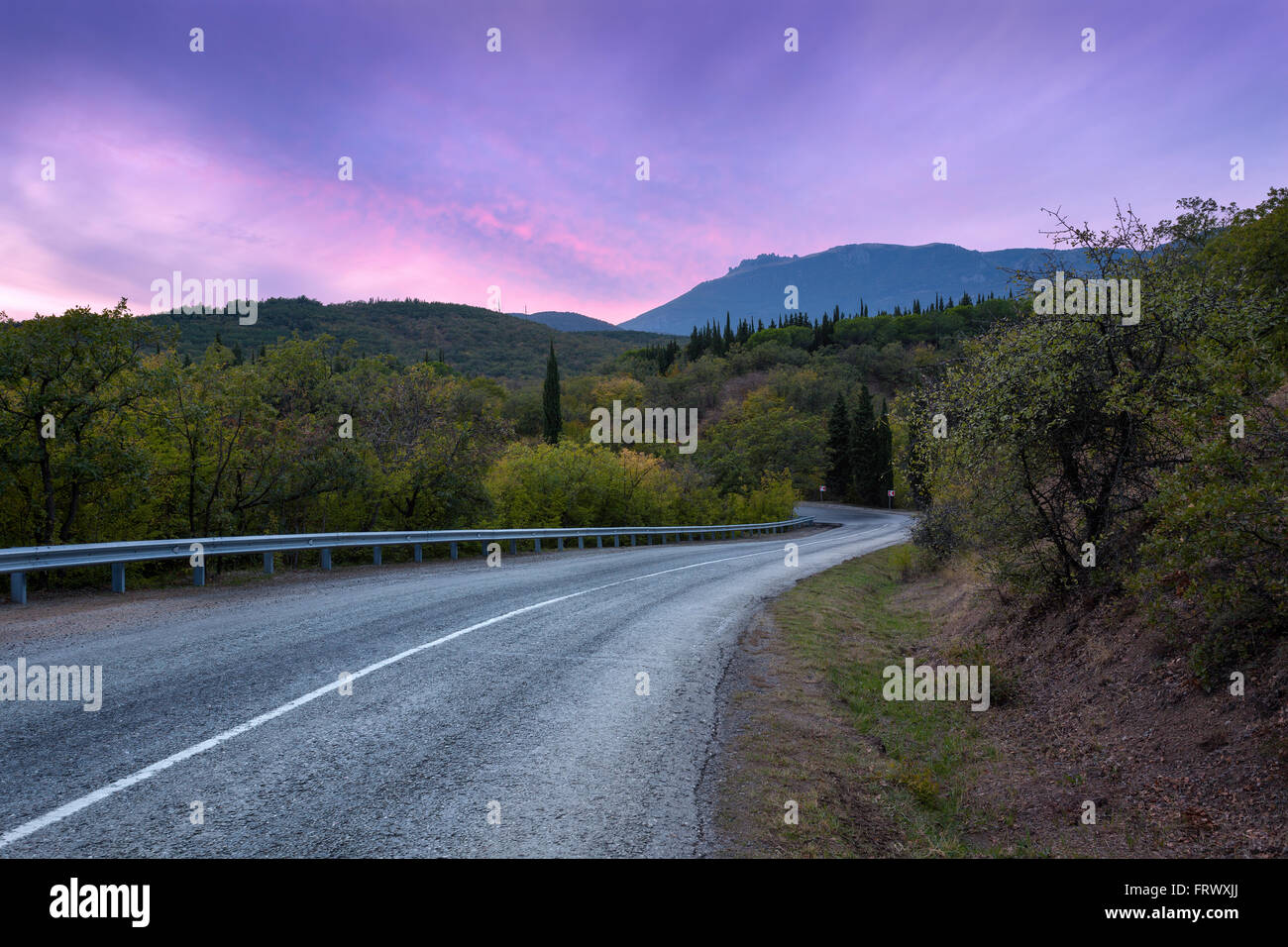 Mountain winding road passing through the forest with colorful sky at sunset in summer Stock Photo