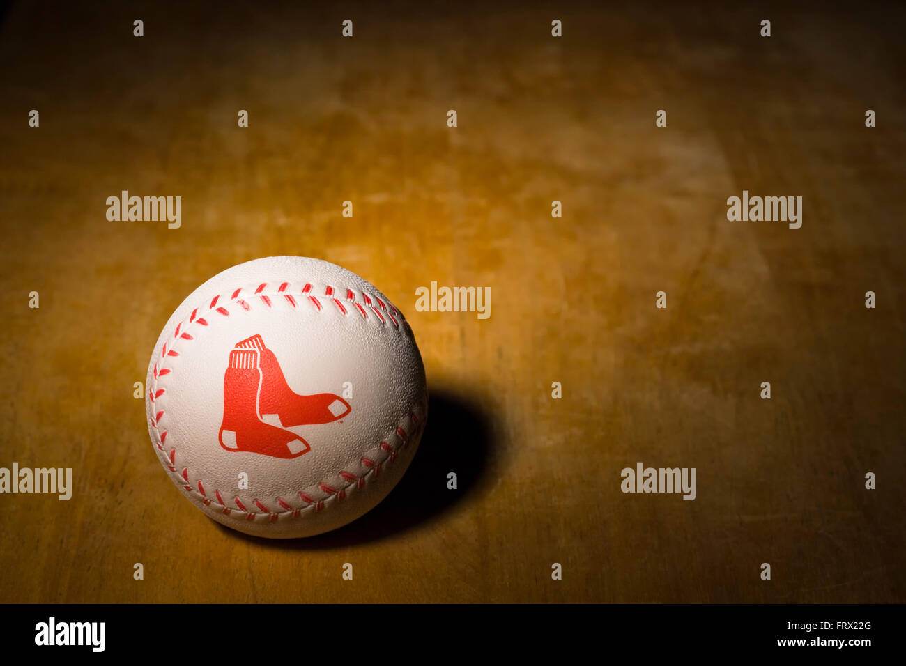 White rubber baseball with the Boston Red Sox logo printed on the side along with red stitching resting on a wooden table Stock Photo