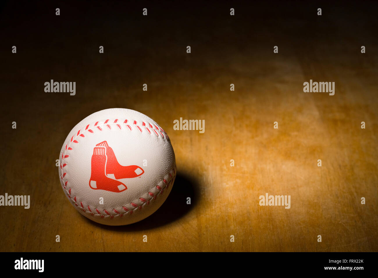 White rubber baseball with the Boston Red Sox logo printed on the side along with red stitching resting on a wooden table Stock Photo