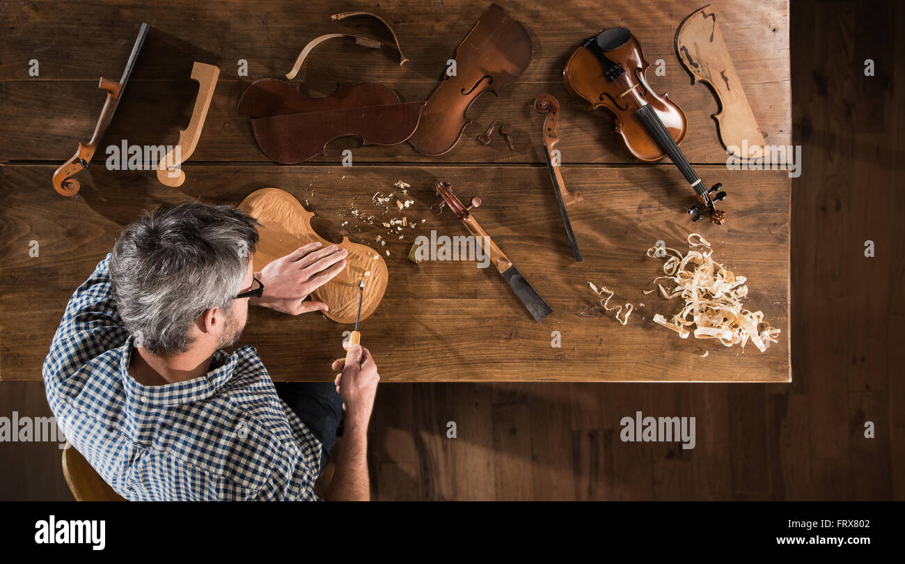 Top view. Artisan luthier working on the creation of a violin. He sits