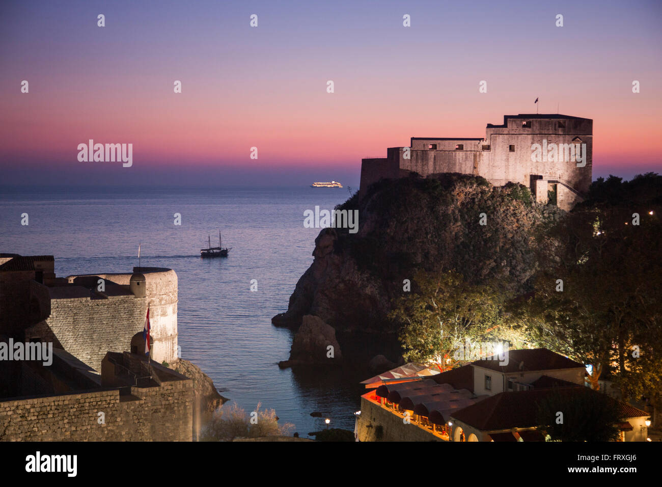 Old town fortification seen from the city wall at dusk with excursion boat and cruise ship in the distance, Dubrovnik, Dubrovnik-Neretva, Croatia Stock Photo