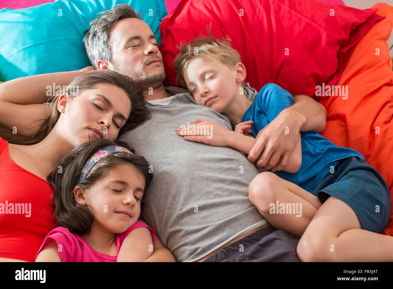 A family is taking a nap all together in a colorful bed with large ...