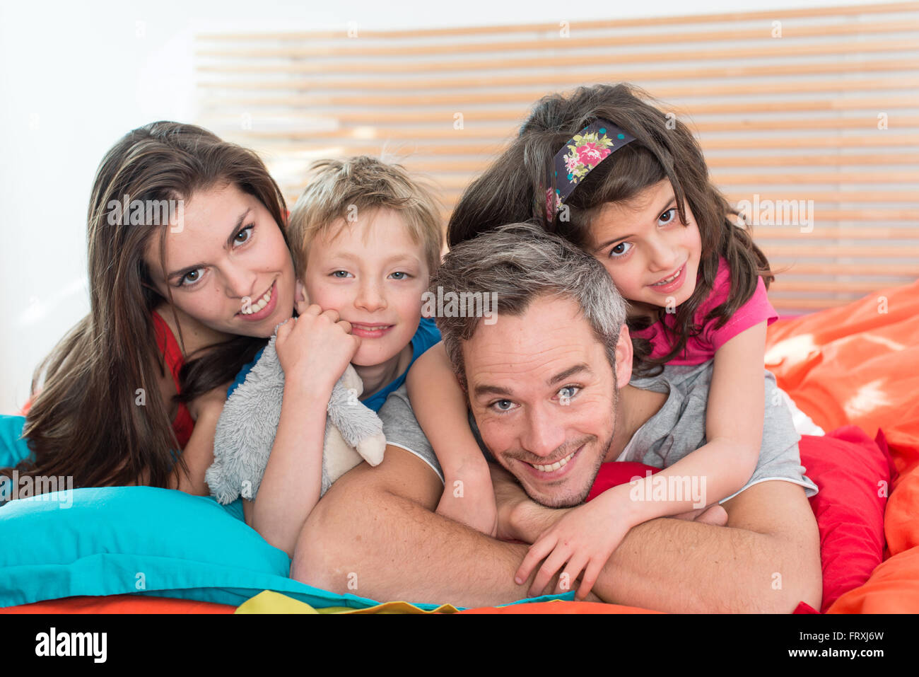 Smiling parents having fun in bed with their two children. The brother and sister are laying on the top of their grey hair father. The blond ten years old boy is holding Smiling parents having fun in bed with their two children. The brother and sister are laying on the top of their grey hair father. The blond ten years old boy is holding