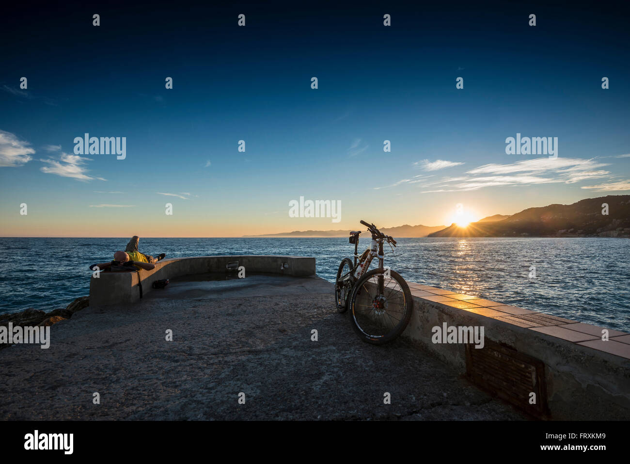 Mountain biker resting on quay wall in sunset, Varigotti, Finale Ligure, Province of Savona, Liguria, Italy Stock Photo