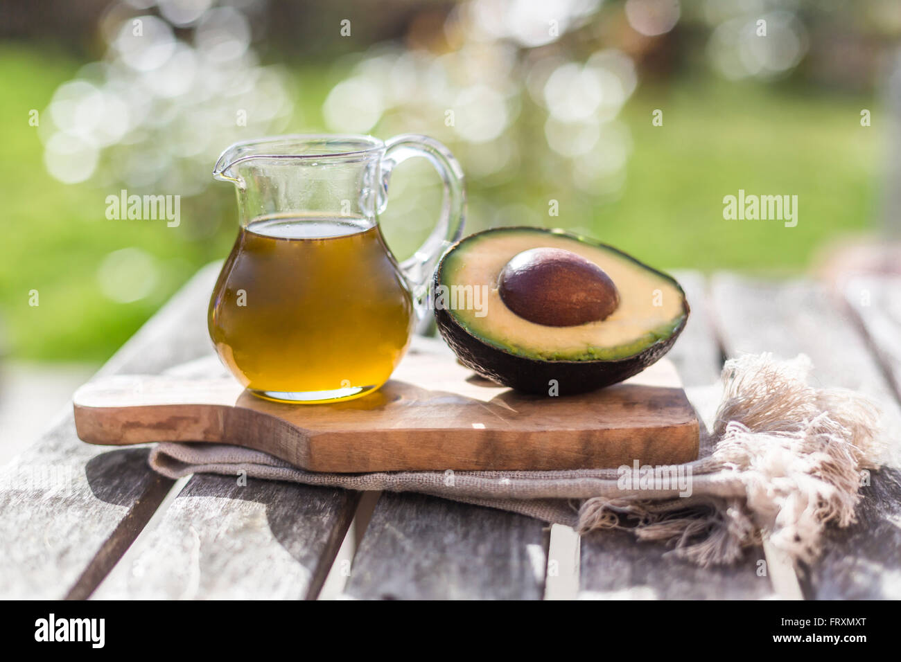 Half of avocado and glass jug of avocado oil on wooden board Stock Photo