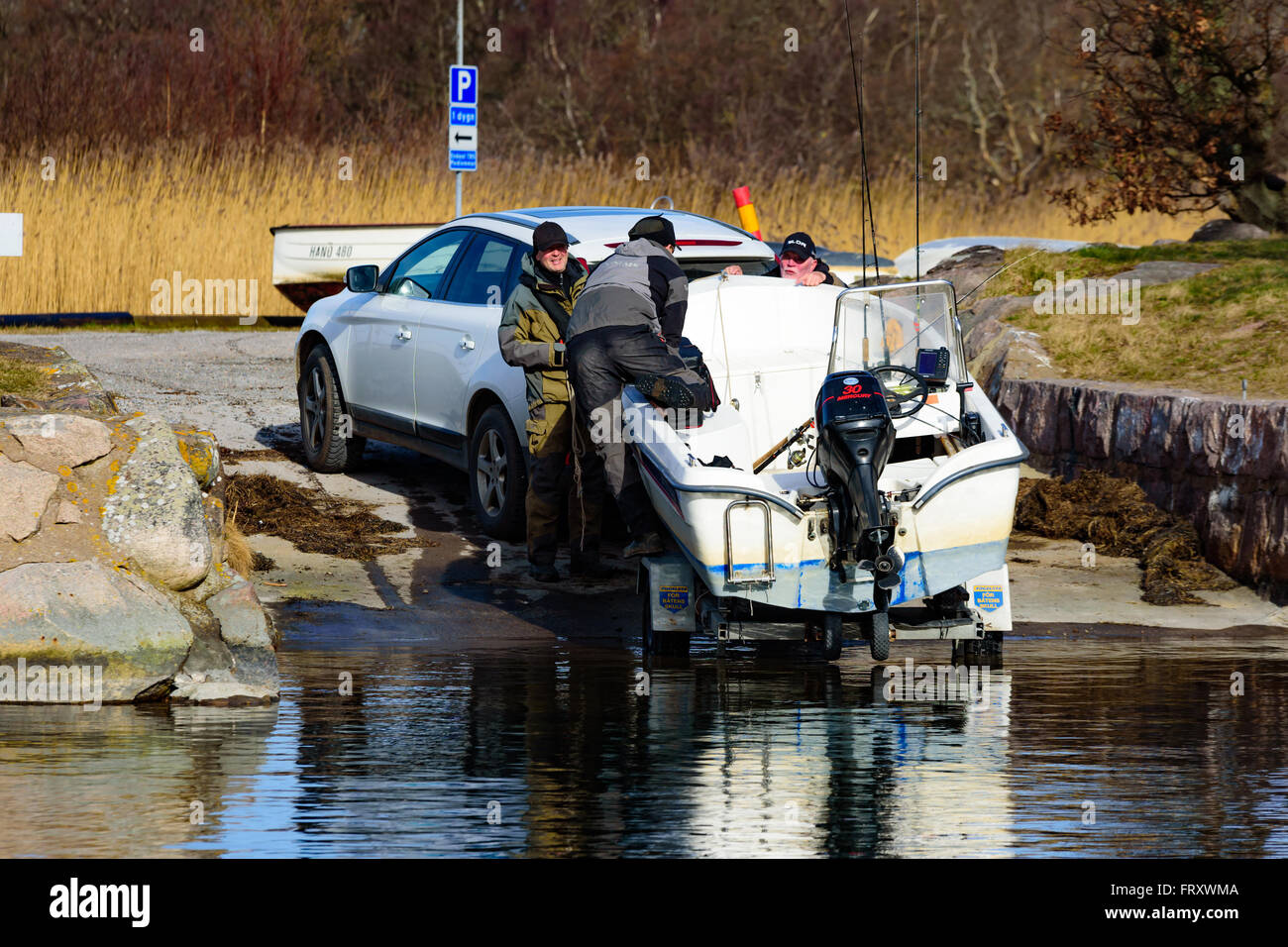 Torhamn, Sweden - March 18, 2016: The launching of a small plastic motor boat at a ramp in the marina. One person climb in to th Stock Photo