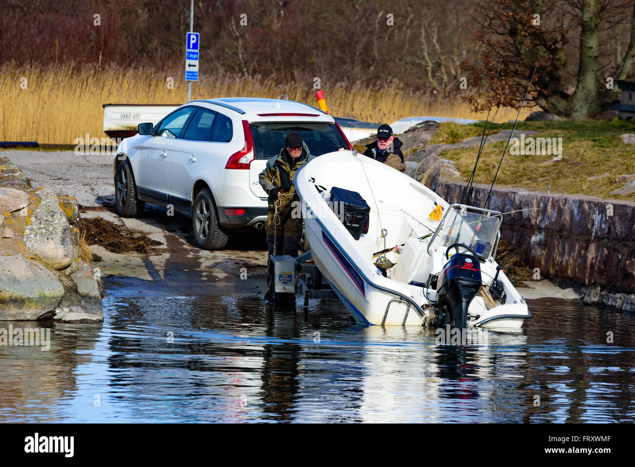 Torhamn, Sweden - March 18, 2016: The launching of a small plastic motor boat at a ramp in the marina. Two men push on the boat Stock Photo