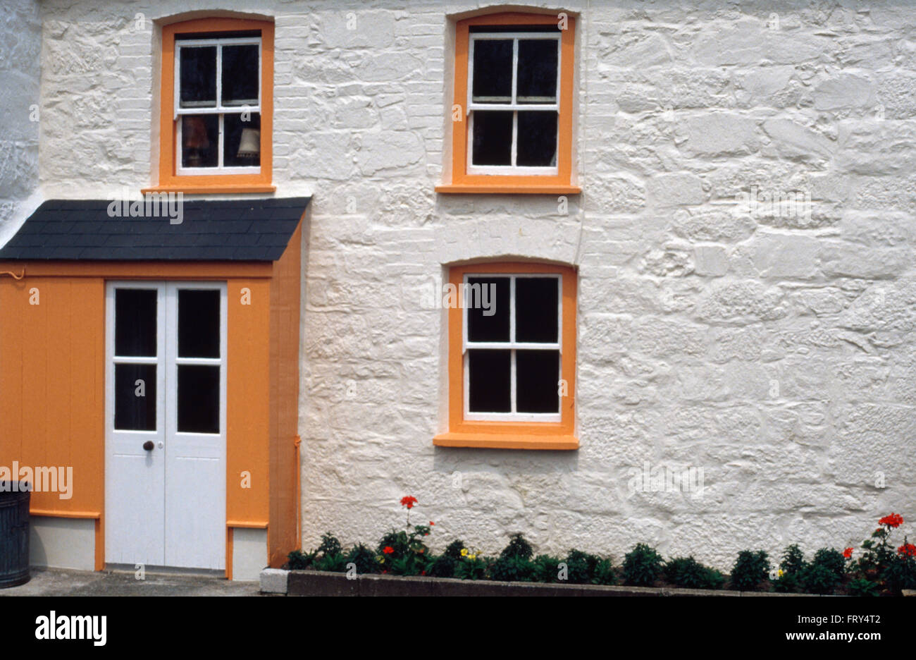 Exterior of a white cottage with orange painted windows Stock Photo