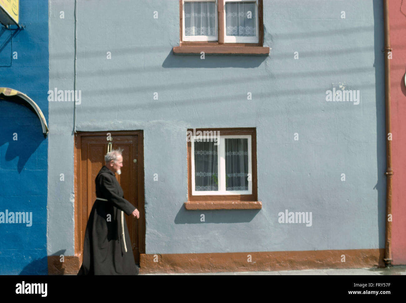 A monk in black robes walking past a blue cottage         FOR EDITORIAL USE ONLY Stock Photo