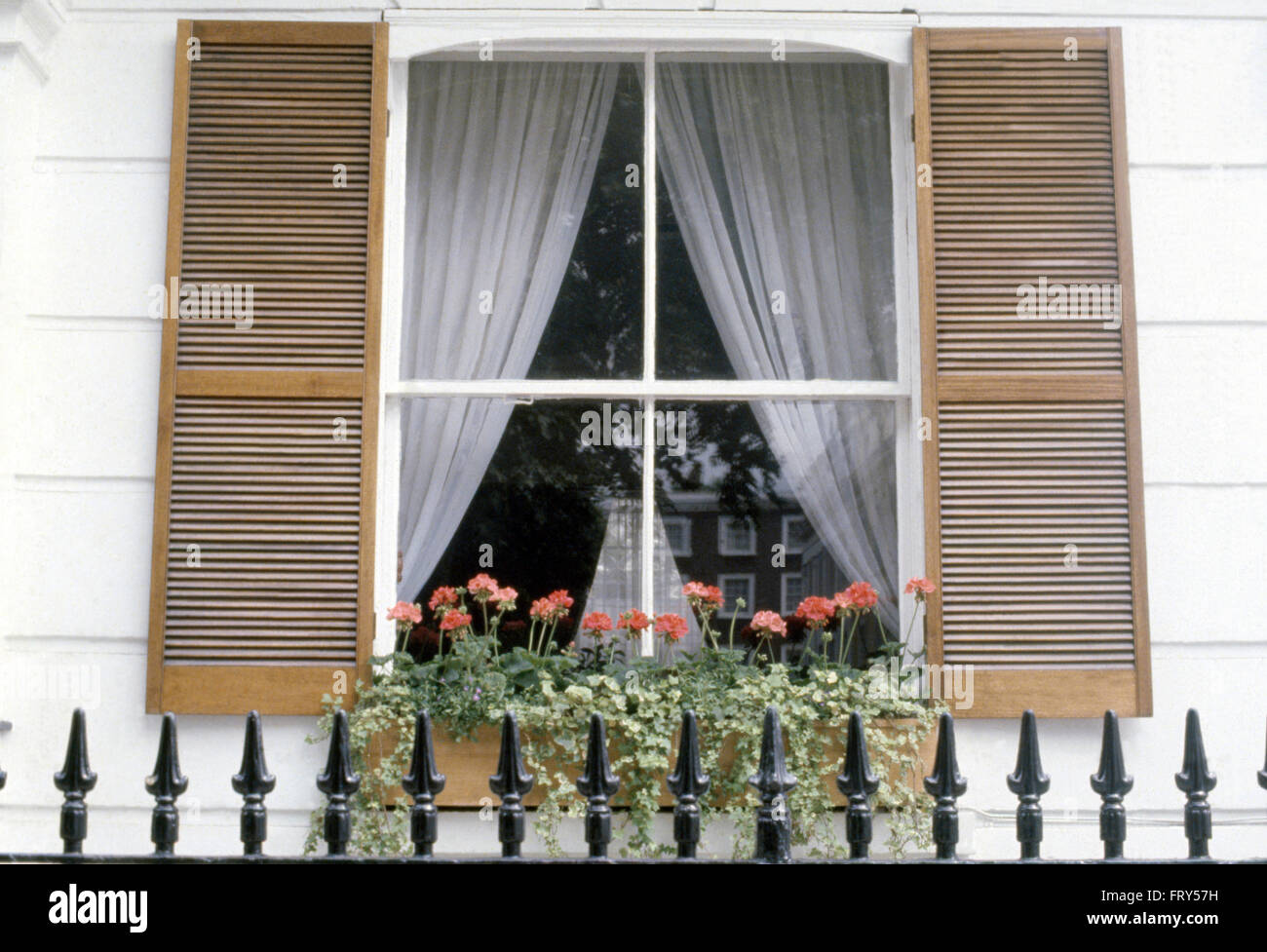 Iron railings in front of house with wooden louvre shutters on window with white curtains Stock Photo