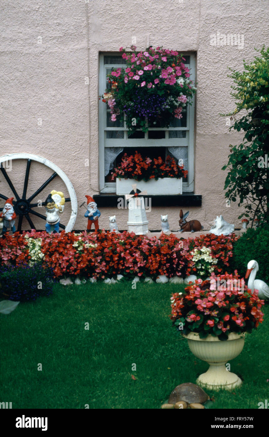 Brightly colored begonias and garden gnomes in suburban front garden of a seventies pink house with pebble dash walls Stock Photo