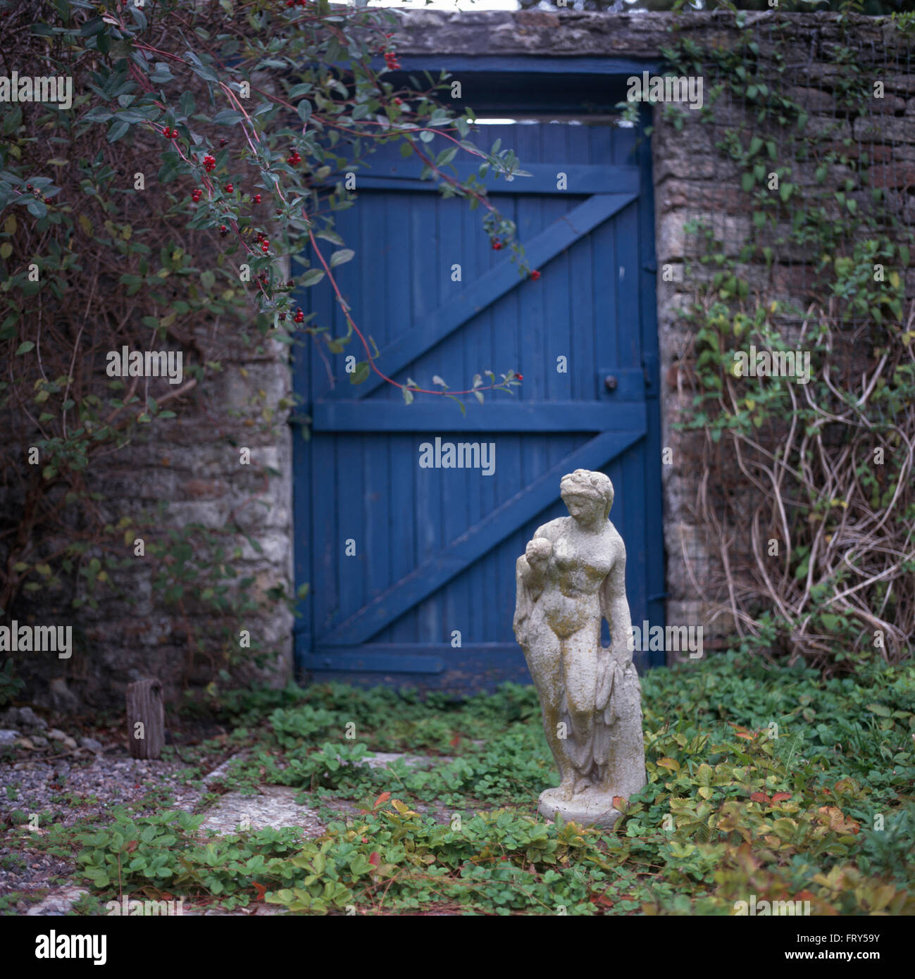 Classical stone statue in front of blue wooden door in a walled country