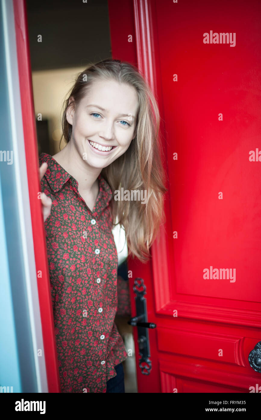 beautiful young woman opening a red door to someone Stock Photo