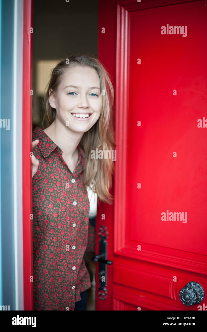 beautiful young woman opening a red door to someone Stock Photo