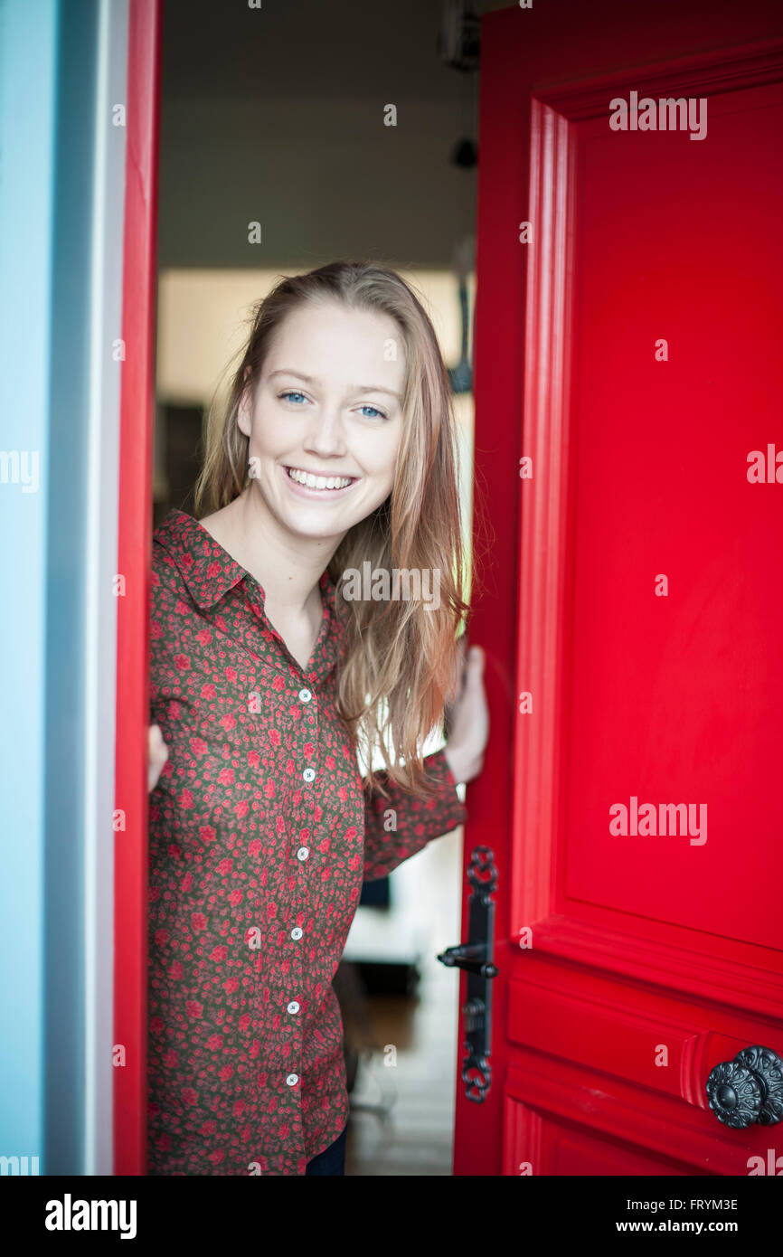 beautiful young woman opening a red door to someone Stock Photo