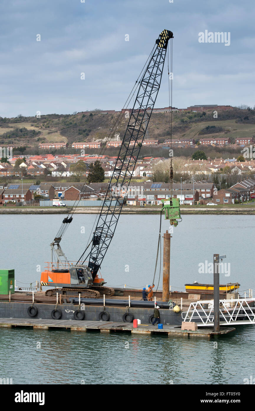 Barge with pile driver constructing pontoons on the coast. Stock Photo