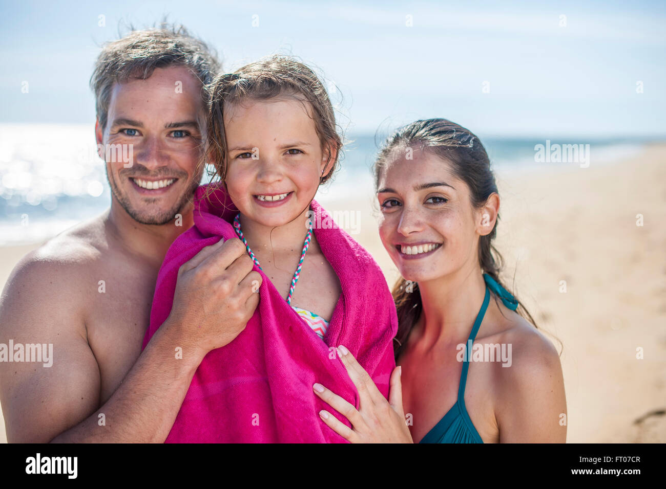 mom and dad on the beach drying their daughter with a beach towel after