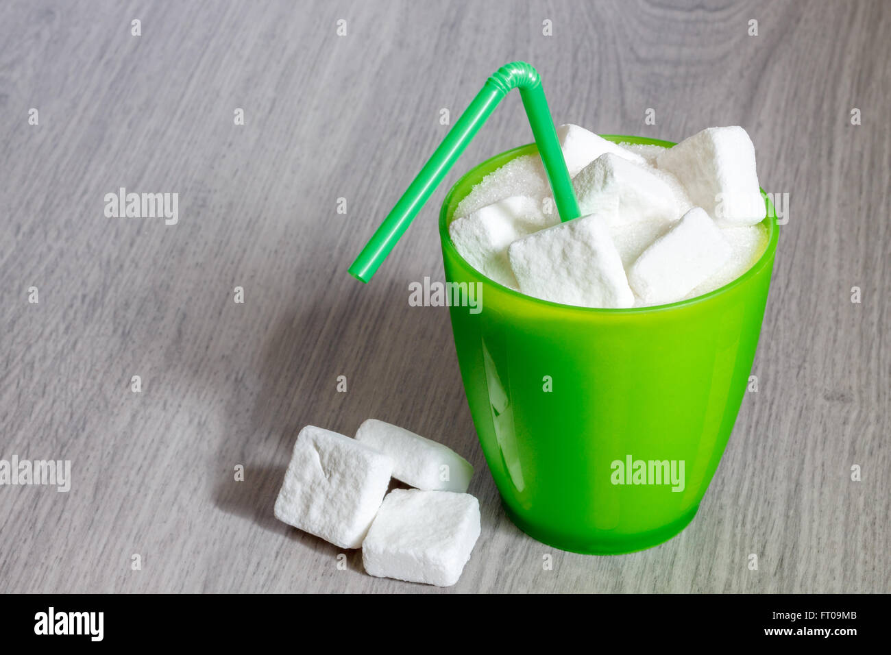 Green plastic glass with straw full of sugar and sugar cubes. Concept image for too much sugar in sodas, juices, beverages, soft Stock Photo